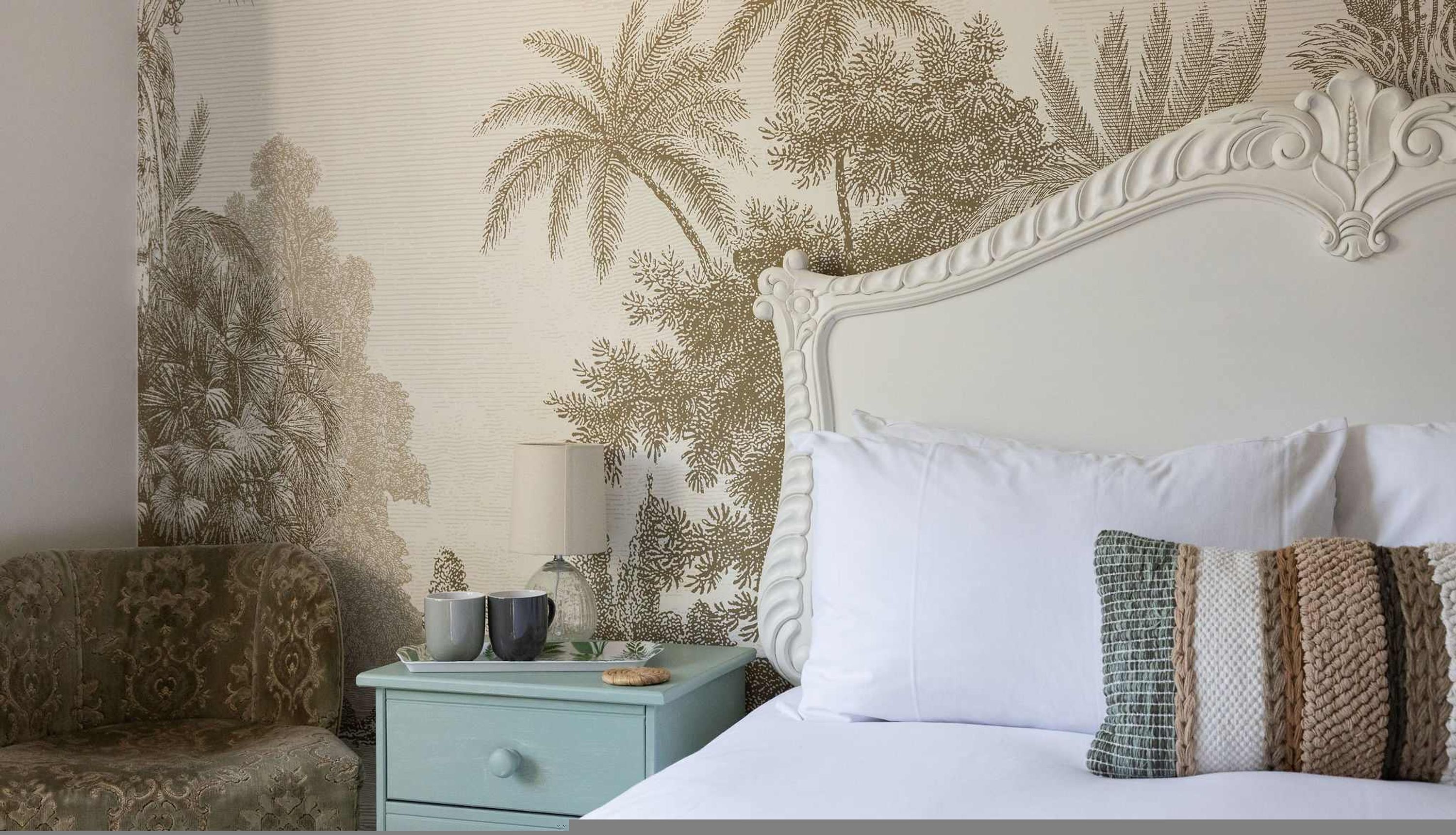 Un dormitorio con cama, almohadas, una mesita de noche, lámpara y una silla.