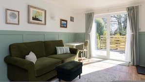 A room with a green sofa, a small table, a chair, and a sliding glass door leading to an outdoor area. - Stylish One Bed Annexe Near Marina and Beaches (Chichester)