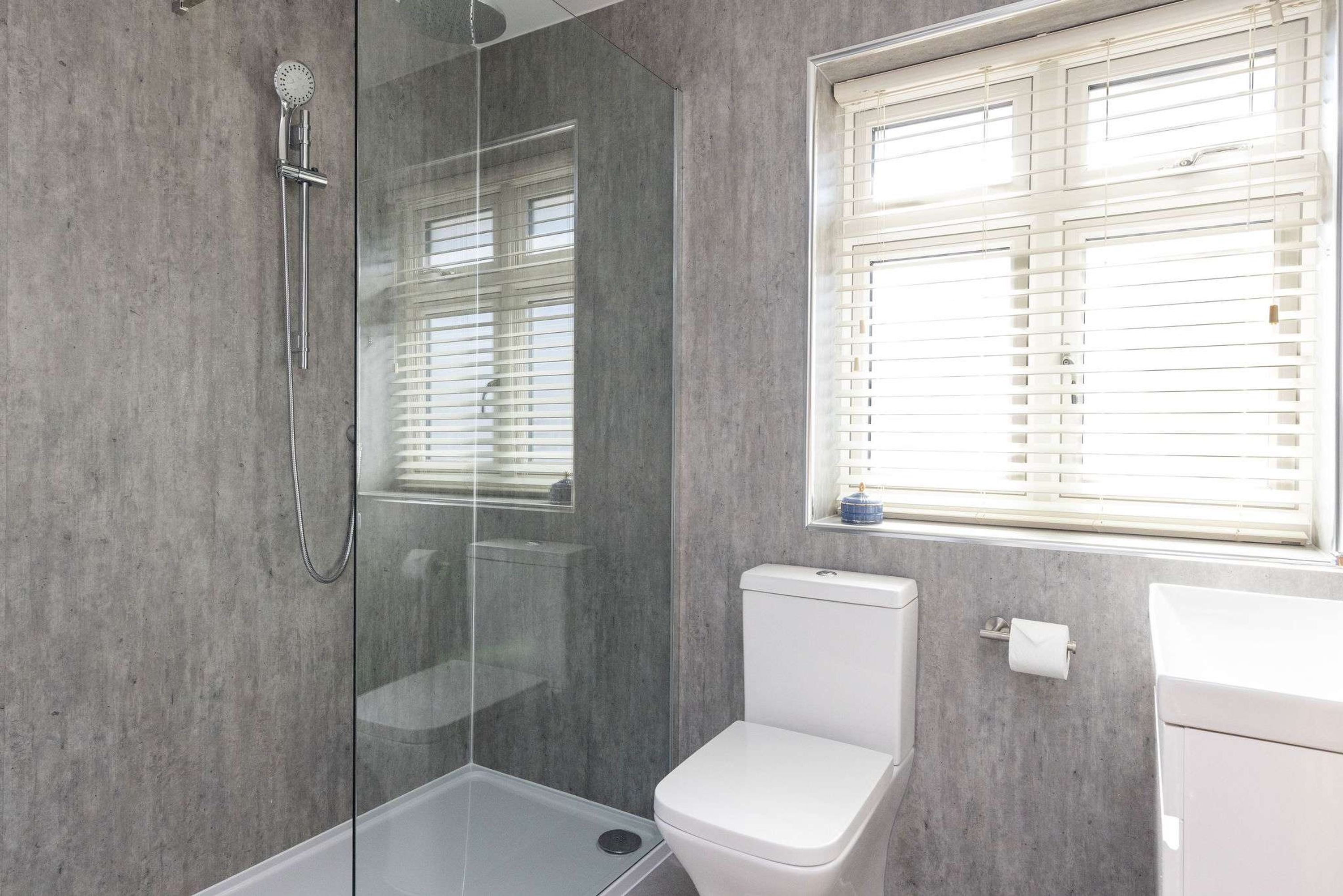 A modern bathroom with a glass-enclosed shower, a toilet, and a window with blinds.