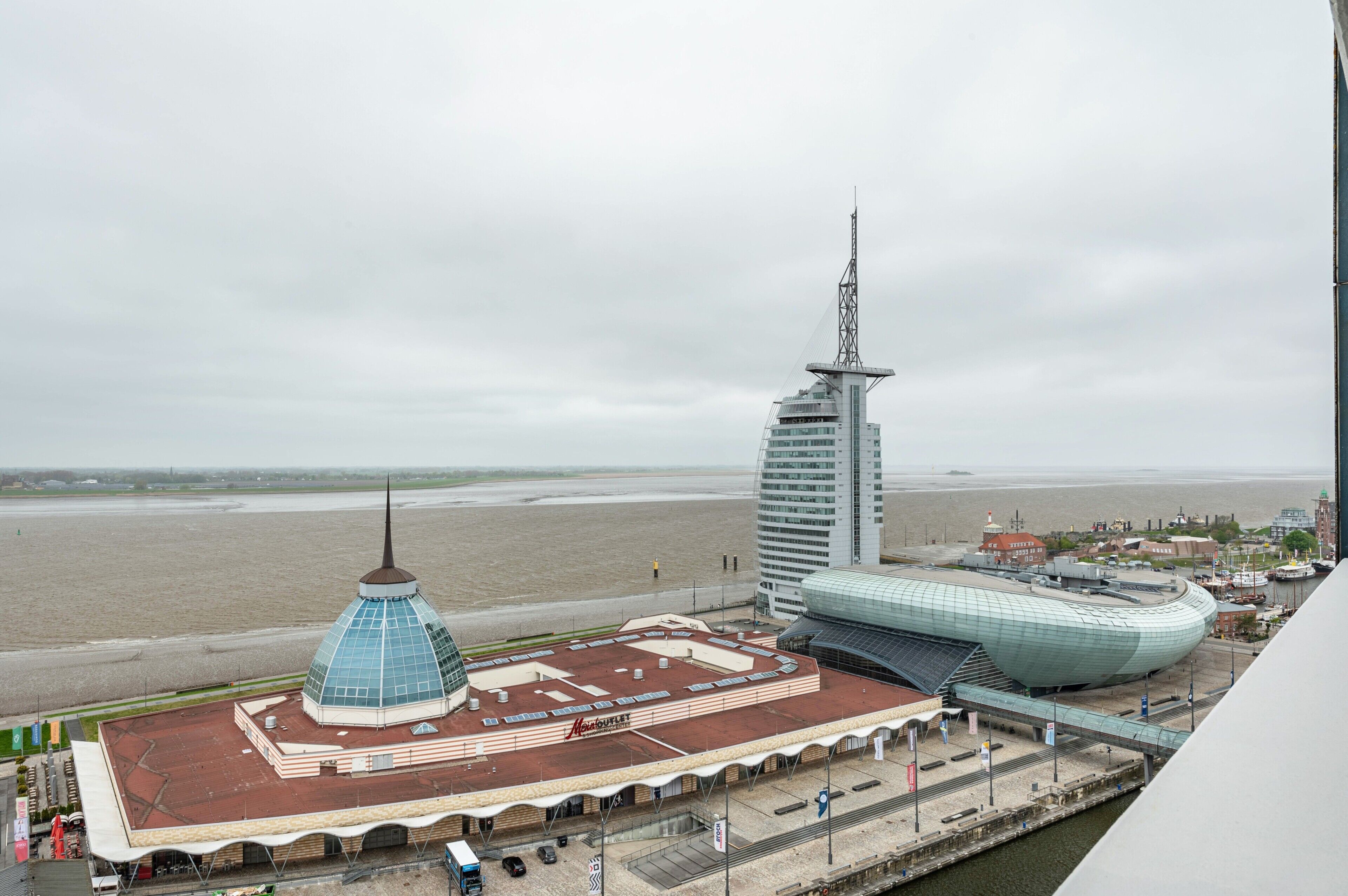 A coastal view with a prominent building with a pointed spire, a large dome structure, and a modern building with a curved roof.