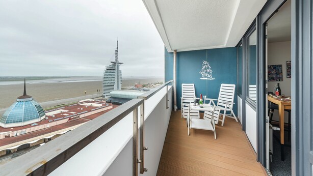 Een balkon met uitzicht op het strand en de stadshemel, een tafel met stoelen en een fles wijn.