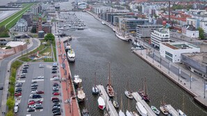 Een jachthaven met aangemeerde boten, een weg parallel aan het water, en gebouwen langs de oever.
