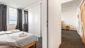 Een hotelkamer met een bed, een klein nachtkastje, een raam met gordijnen en een deur naar een andere kamer.