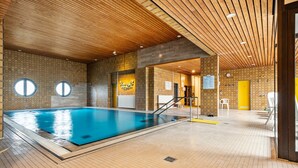 Een binnenzwembad met houten plafond, betegelde wanden en een gele deur.