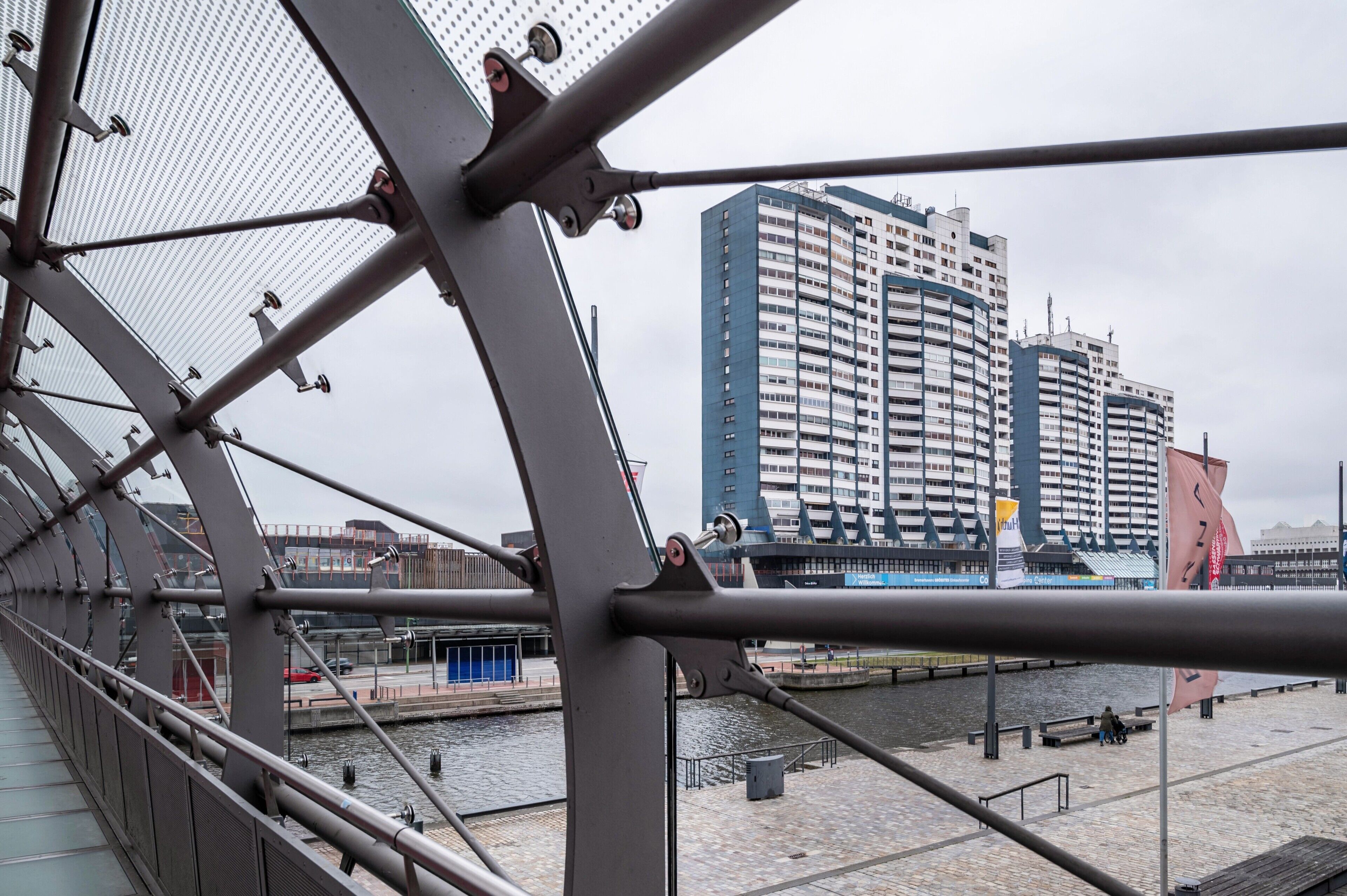A bridge with metal railings and a view of a waterfront with buildings and a flag.