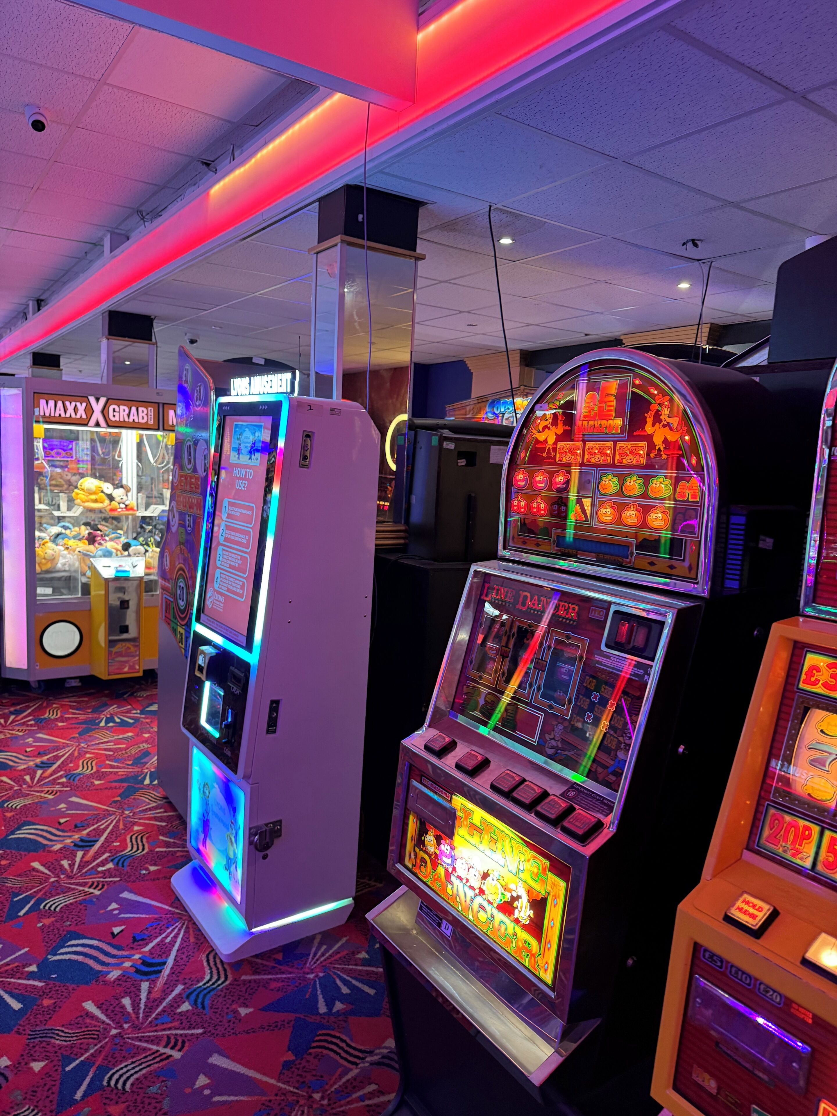 Une rangée de machines à sous aux écrans colorés et attrayants, un plafond équipé d’une caméra de surveillance et un tapis à motifs.