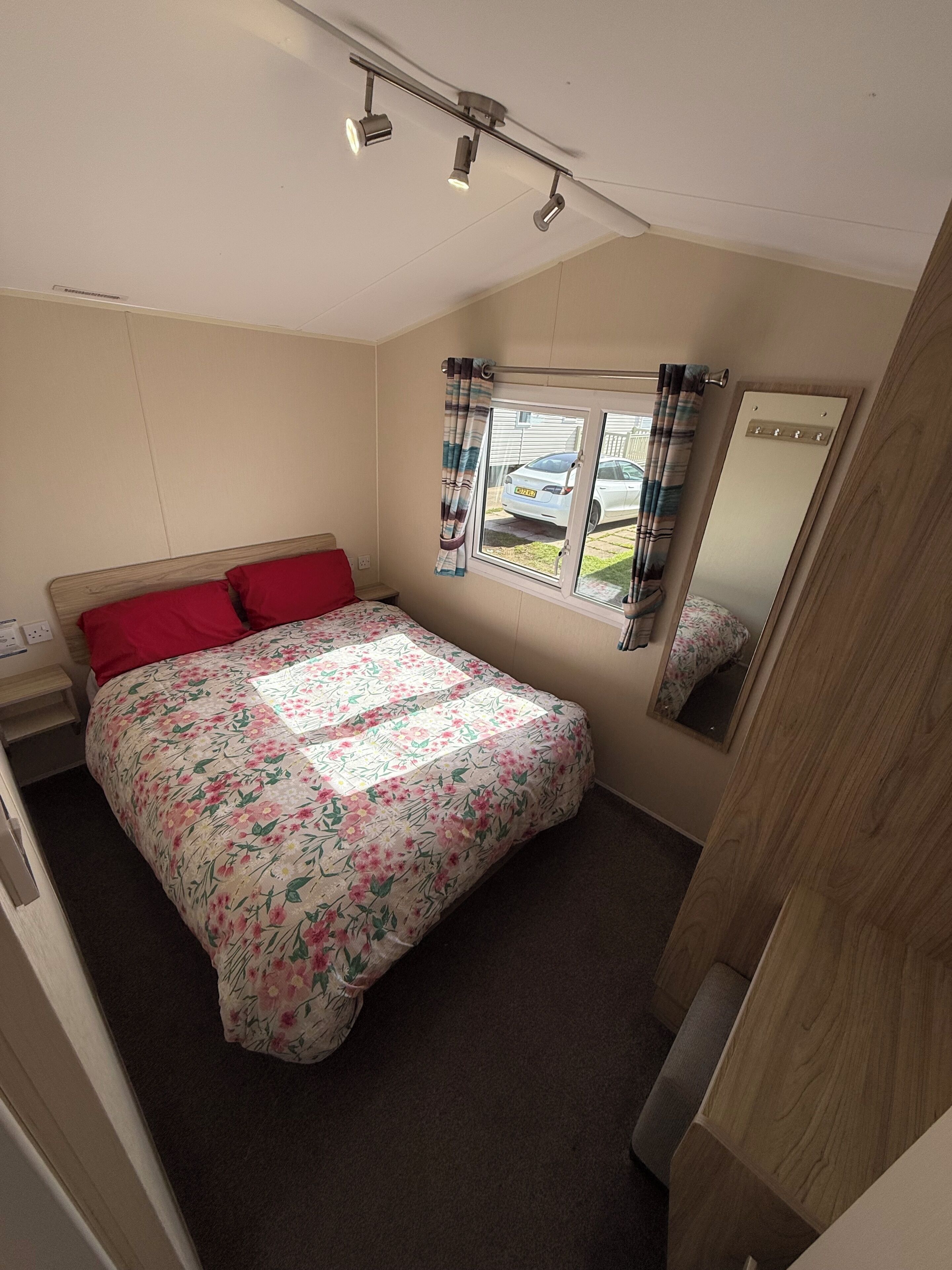 Een slaapkamer met een bed, een raam met gordijnen, een spiegel en een plafondlamp.