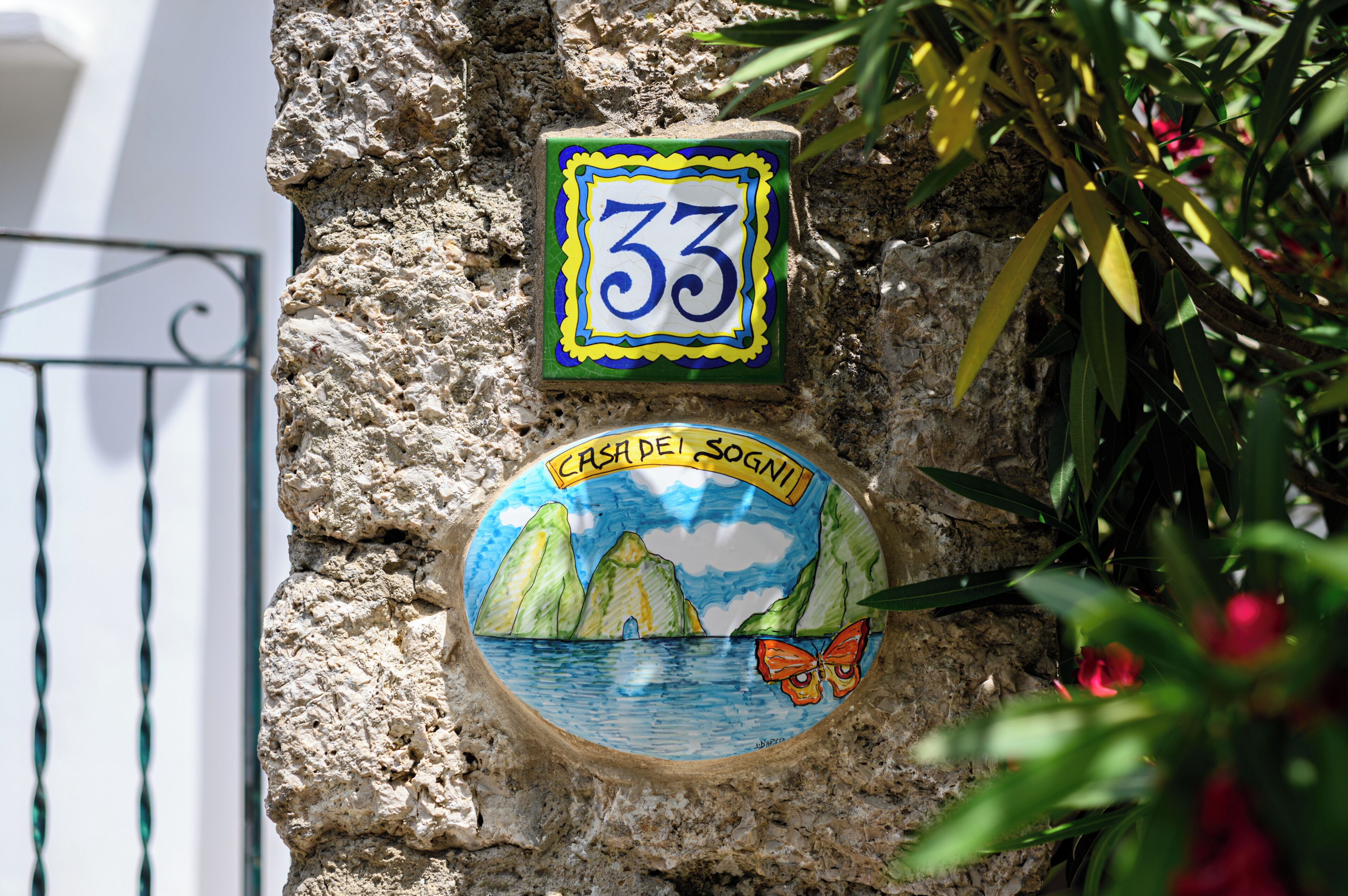 Un muro de piedra con dos letreros decorativos: uno con el número 33 y otro con un paisaje y una mariposa.