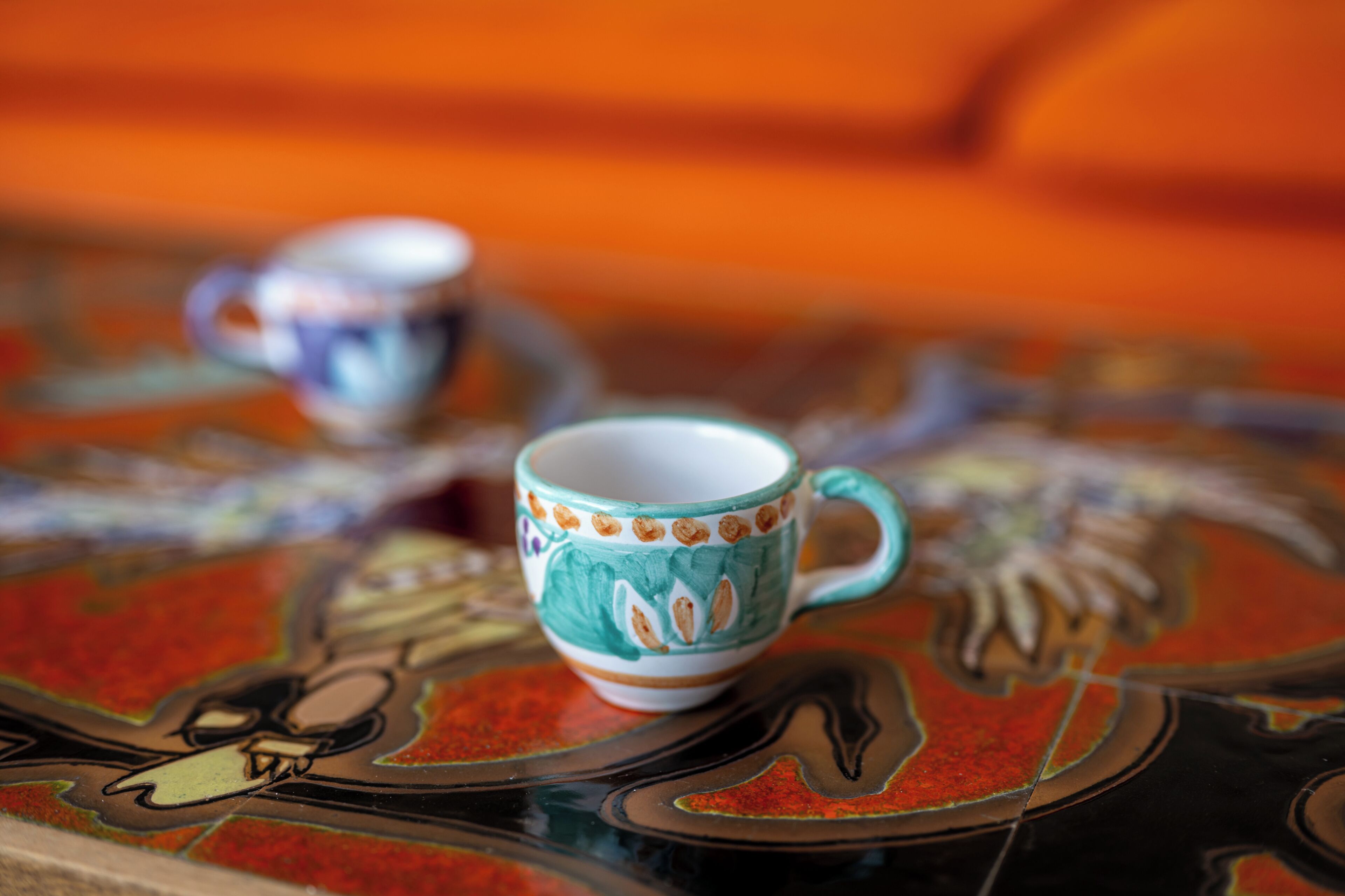 A table with a colorful, patterned tablecloth and two ceramic cups.