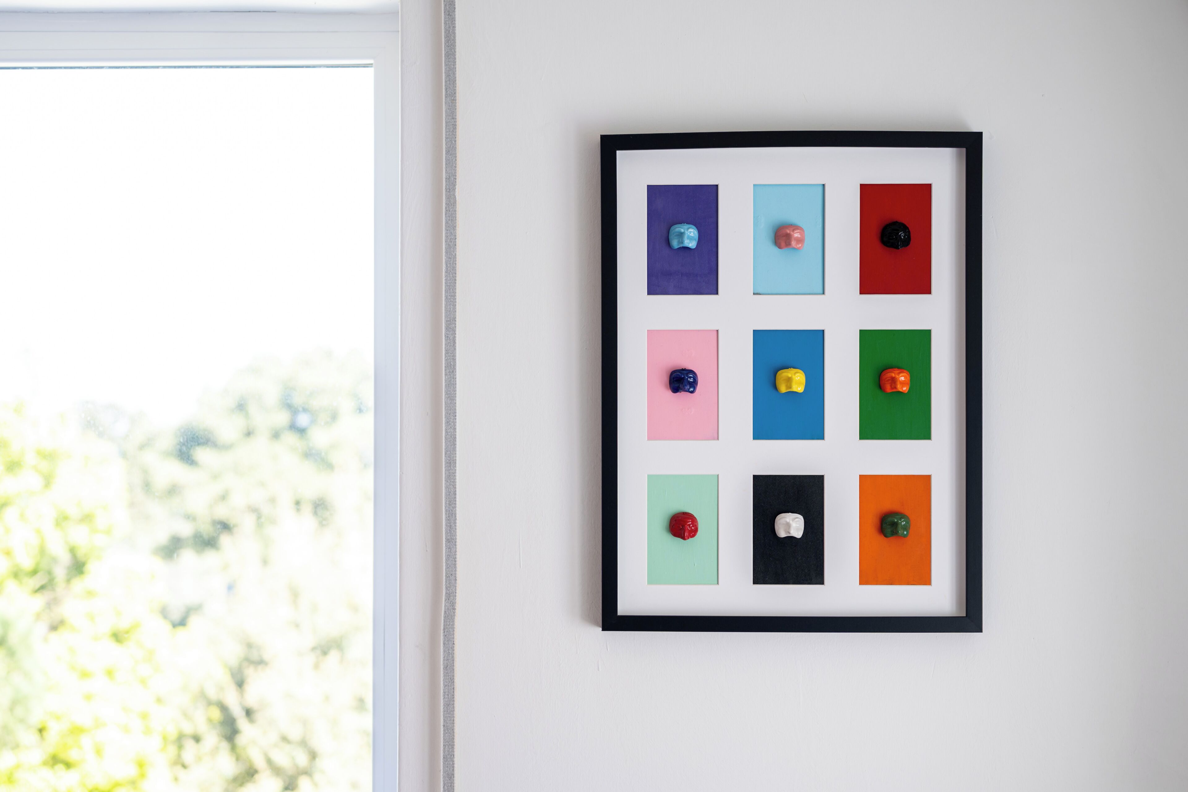 Ein gerahmtes Kunstwerk mit mehreren farbigen Quadraten an einer weißen Wand.