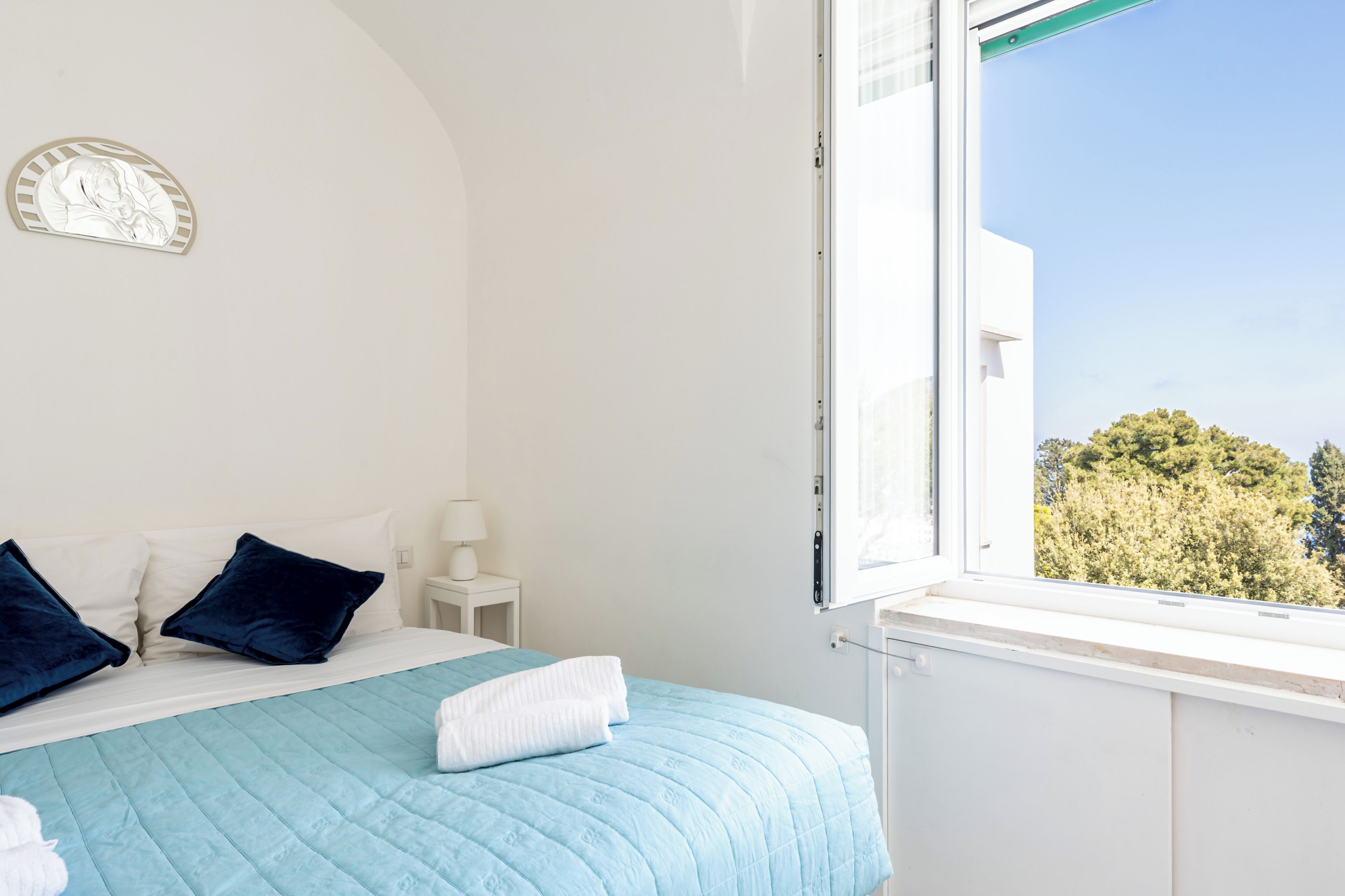 A bedroom with a bed, pillows, a nightstand, a window, and a wall decoration.