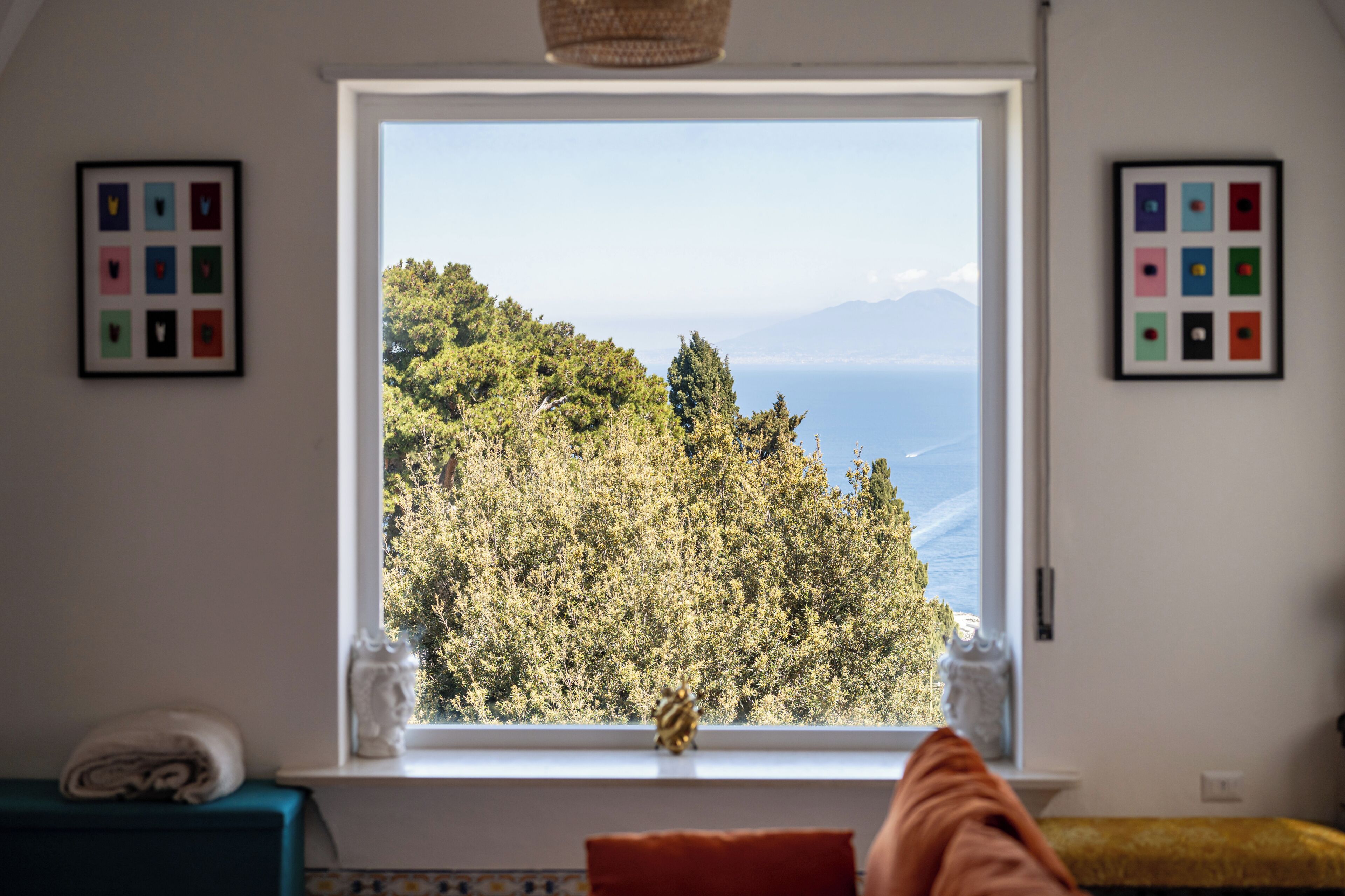 A room with a large window, a view of a forested hillside, and two framed artworks on the walls.