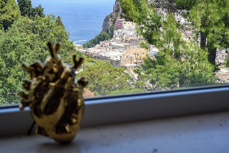 A coastal town with buildings on a hillside, a clear view of the sea, and a window sill with a decorative object.