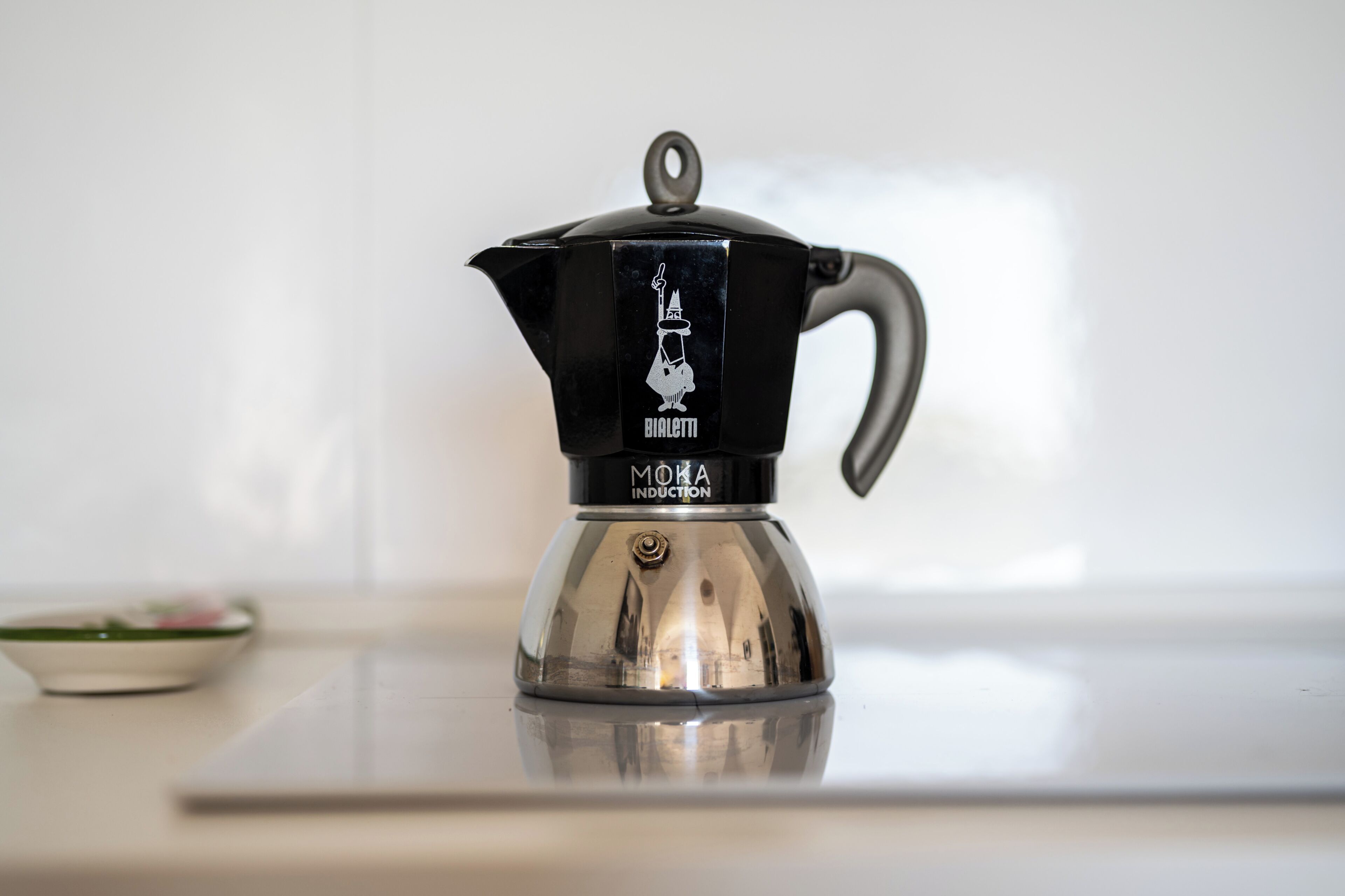 Una cafetera moka d'inducció sobre una superfície reflectant.