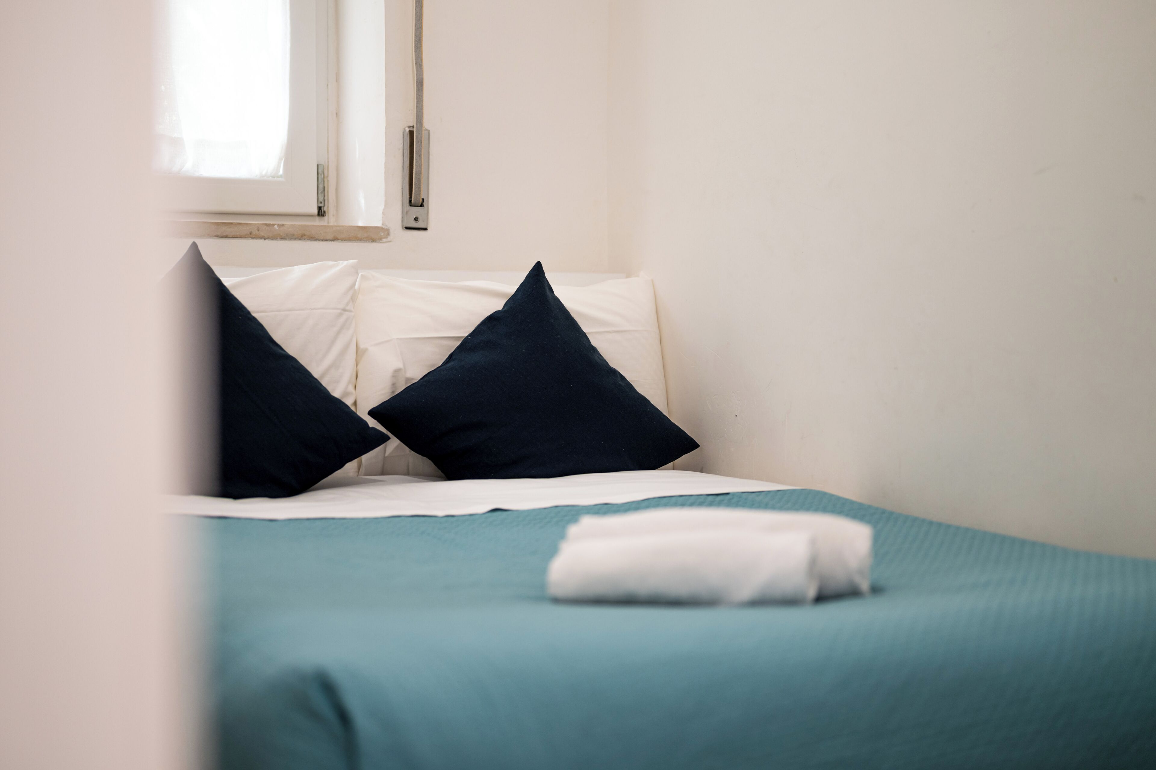 Una cama con colcha color turquesa, dos almohadas y una manta blanca.