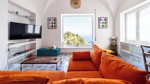 Een woonkamer met een televisie, bank en uitzicht op zee.