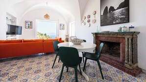 Een moderne woonkamer met een bank, een ronde tafel, stoelen, een open haard en een groot raam.