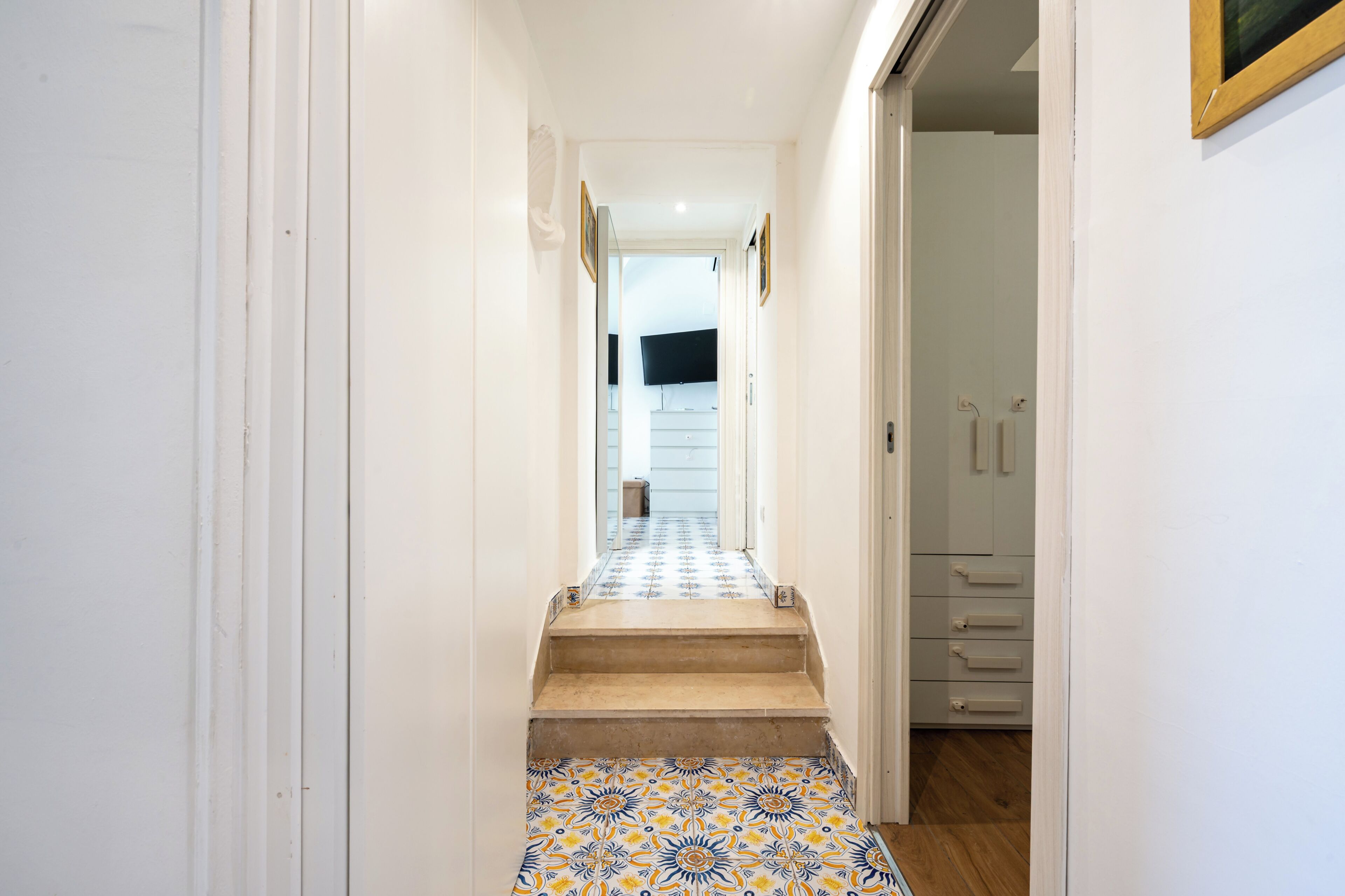 Un pasillo con piso estampado, una escalera y una puerta que da a una habitación con televisión de pantalla plana.
