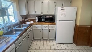 Una cocina con armarios blancos, un refrigerador, un microondas y una encimera de madera.