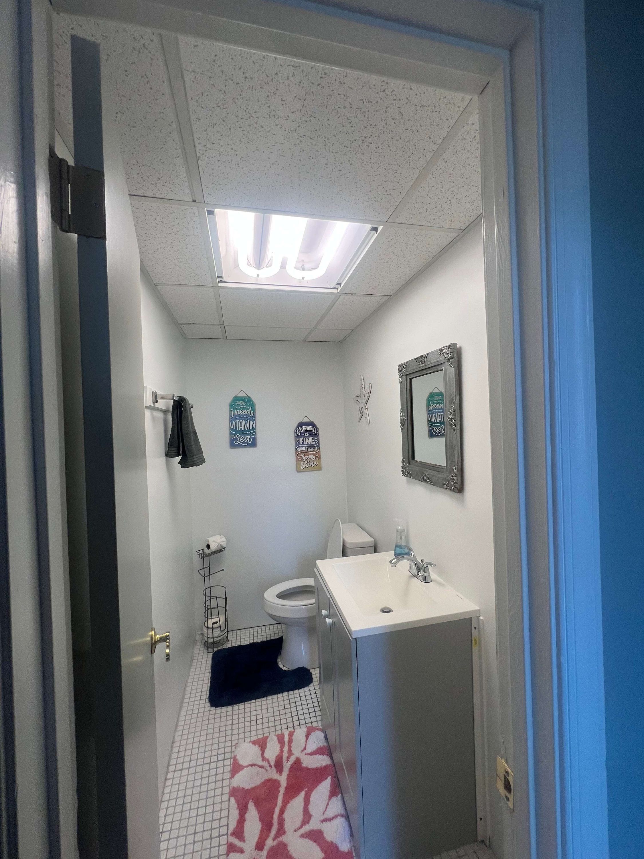 Un baño con inodoro, lavamanos, toallero y espejo.