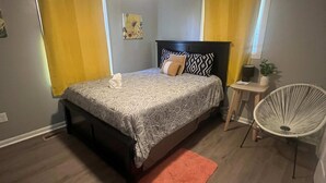 Un dormitorio con una cama, un ventilador de techo, una mesita con una planta y una silla.