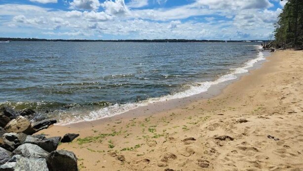 Una playa con cielos despejados, agua tranquila y un litoral rocoso.