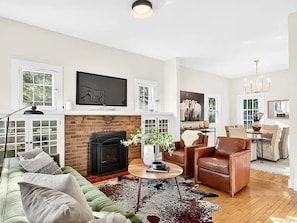 A living room with a fireplace, green sofa, leather armchair, and a dining area with a chandelier. - Spacious Linden Hills 4BD 2A Family Home (Minneapolis)