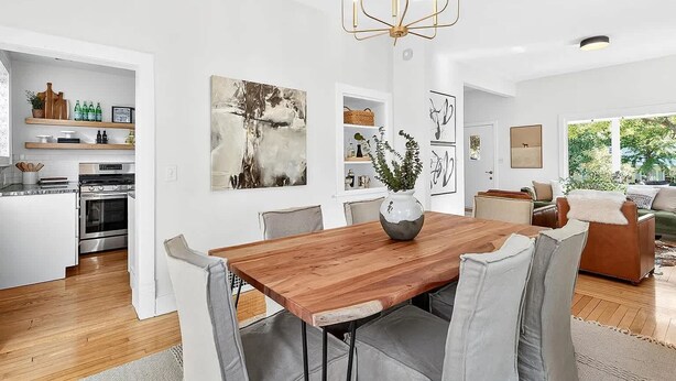 A modern kitchen with a dining area, featuring a wooden table, grey upholstered chairs, and a chandelier. - Spacious Linden Hills 4BD 2A Family Home (Minneapolis)