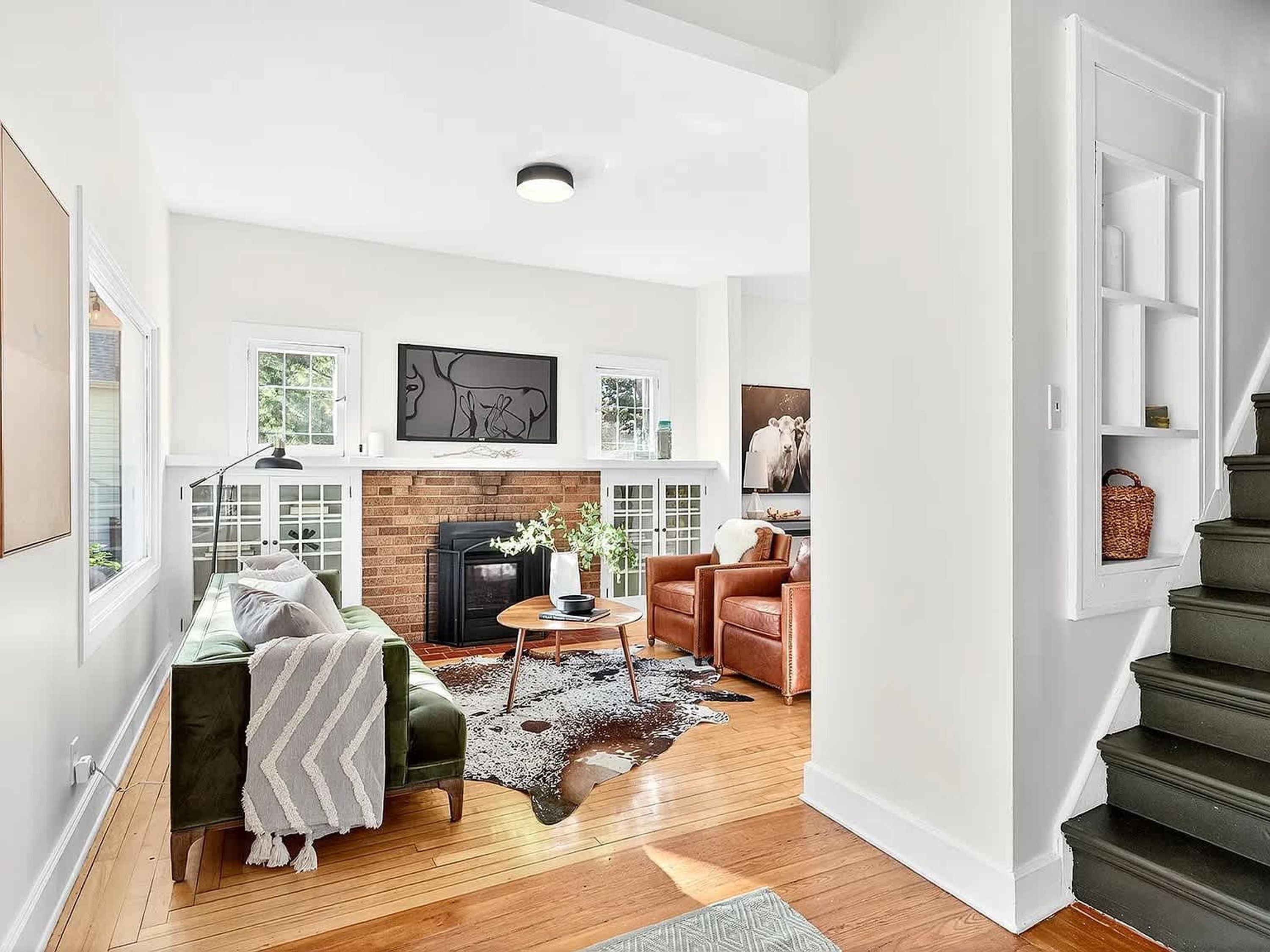 A spacious living room with a fireplace, a staircase, and a view of the outdoors.