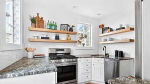 A modern kitchen with white cabinets, a stainless steel stove, wooden shelves, and a window. - Spacious Linden Hills 4BD 2A Family Home (Minneapolis)