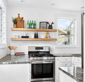 A kitchen with white cabinets, a stainless steel stove, and wooden shelves above holding bottles and kitchenware. - Spacious Linden Hills 4BD 2A Family Home (Minneapolis)