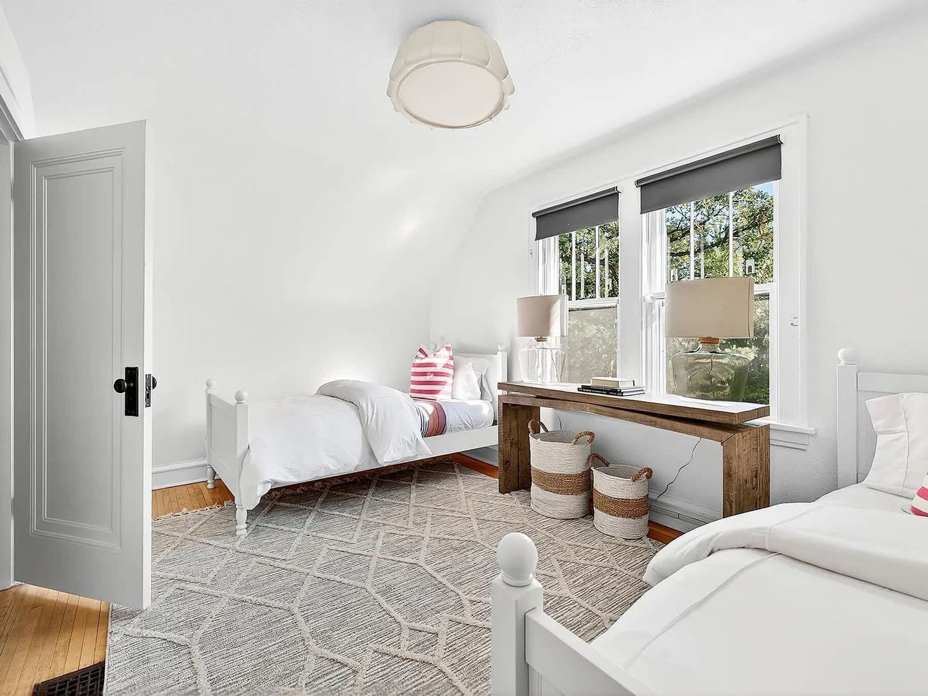 A bedroom with a bed, bedside table, lamp, window, and a view of greenery outside.