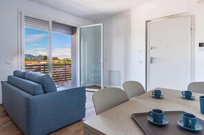 A modern room with a sofa, a dining table with cups, and a sliding glass door leading to an outdoor area. - Balcony Tower View - Modern Apartment with Private Parking (Pisa)