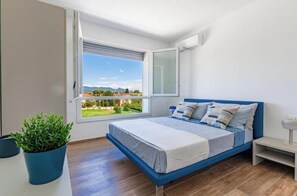 Um quarto com cama, janela, planta e mesa de cabeceira.