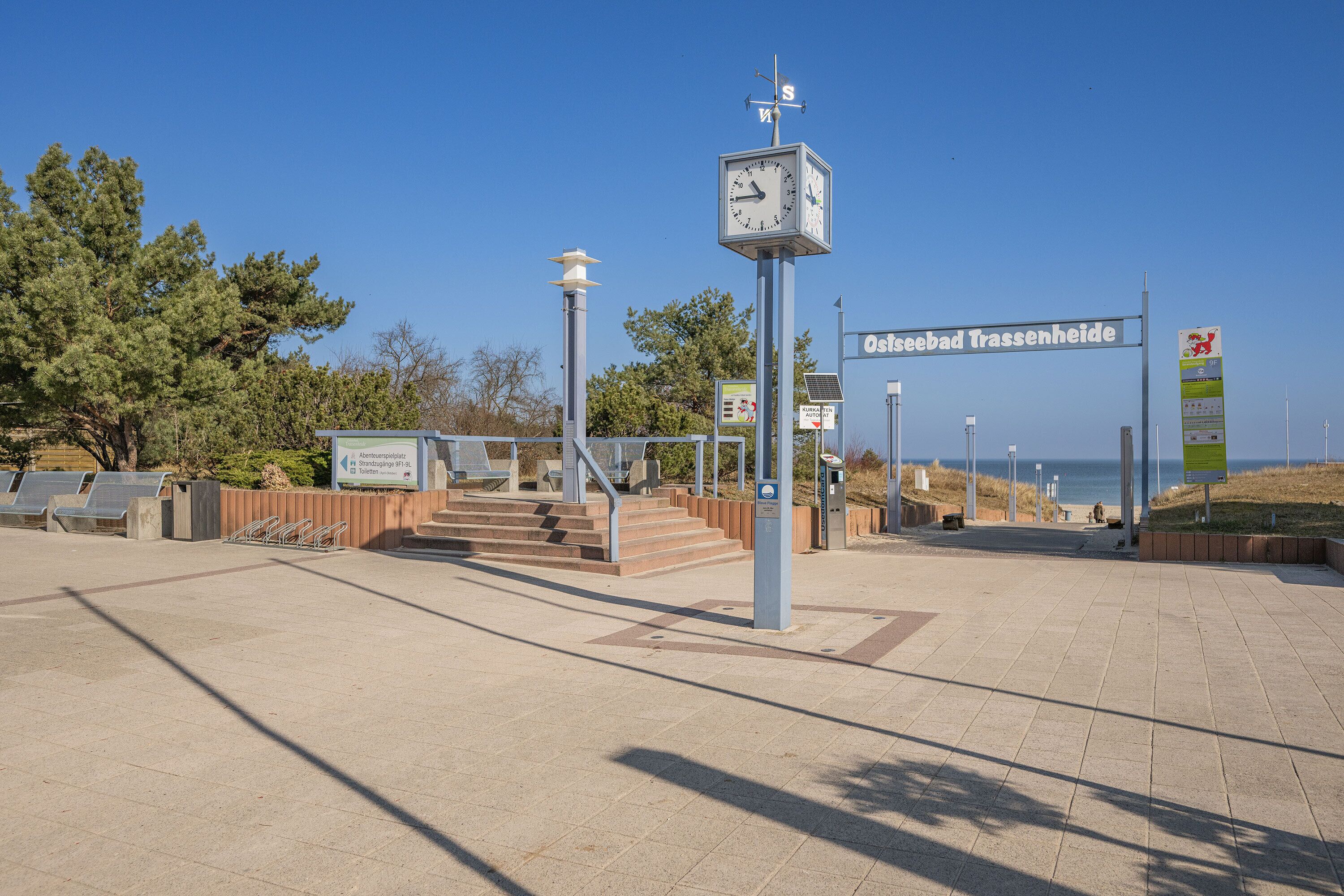 Kellotorni, portaikko ja kyltti, jossa lukee ”Ostseebad Trassenheide”, selkeässä ja aurinkoisessa ympäristössä.