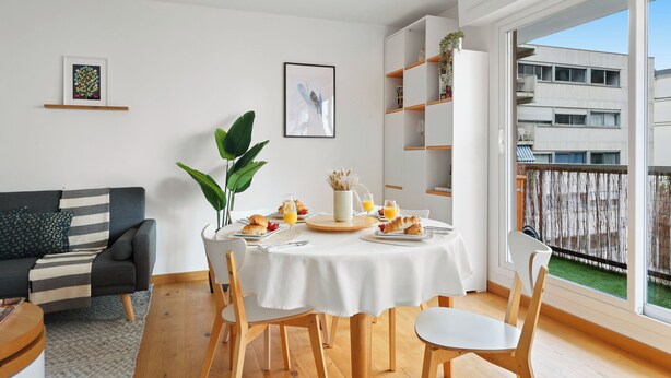 A modern dining area with a round table, chairs, and breakfast items. There is a sofa and a bookshelf in the background. - Cozy 2BR Eiffel Tower Area (Paris)