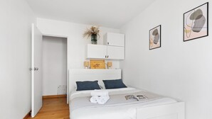 A bedroom with a bed, white walls, a wooden floor, a wardrobe, and two framed pictures. - Cozy 2BR Eiffel Tower Area (Paris)