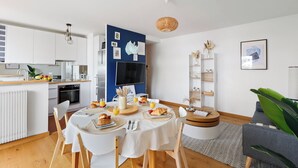 A modern kitchen with white cabinets, a dining table set with plates, and a TV mounted on the wall. - Cozy 2BR Eiffel Tower Area (Paris)