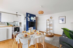 A modern kitchen with white cabinets, a dining table set with plates, and a TV mounted on the wall. - Cozy 2BR Eiffel Tower Area (Paris)