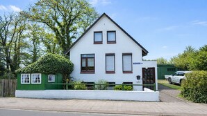 A two-story house with a white facade, a green fence, and a car parked in the driveway. - Your perfect time-out in Duhnen - cozy, central and close to the beach (Cuxhaven)