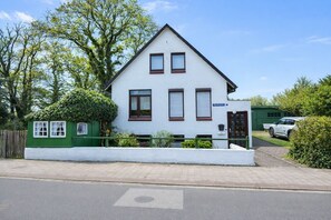 Ein zweistöckiges Haus mit weißer Fassade, einem grünen Zaun und einem Auto auf der Auffahrt.