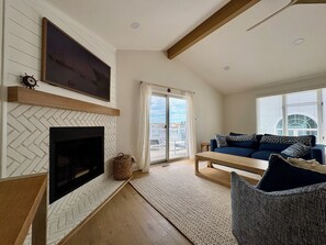 A living room with a fireplace, a sofa, a bench, and a view through a glass door. - Beautifully Renovated 4br Home on Avalon - Stone Harbor Border - Pet Friendly (Avalon)