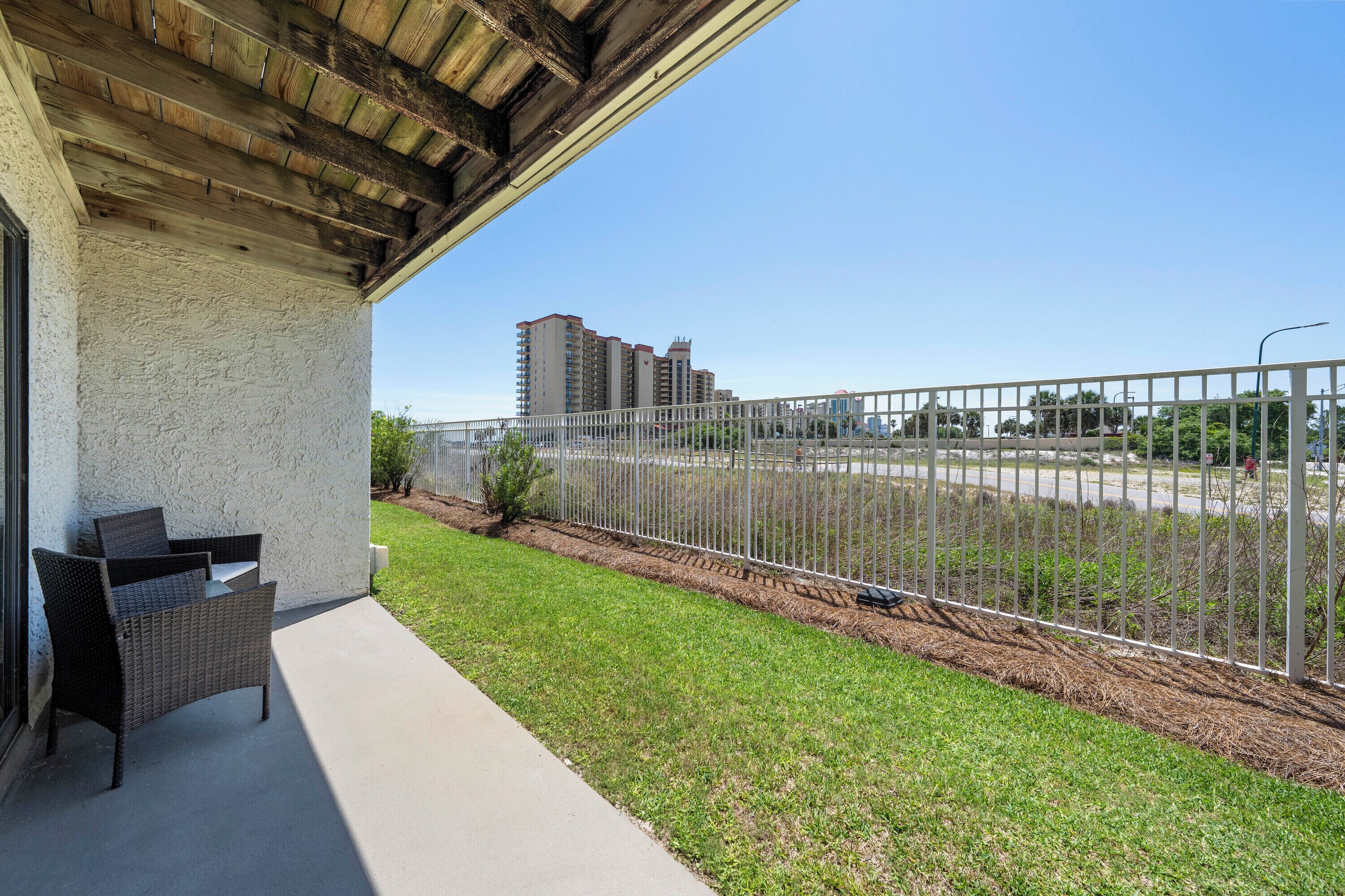A covered patio with a wicker chair, a concrete floor, a metal fence, and a view of distant buildings.