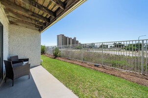 A covered patio with a wicker chair, a concrete floor, a metal fence, and a view of distant buildings.