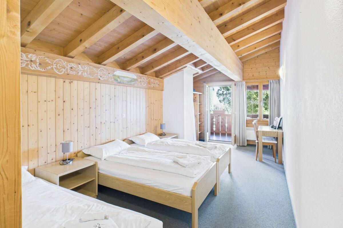 A wooden cabin with two beds, a desk, and a balcony.