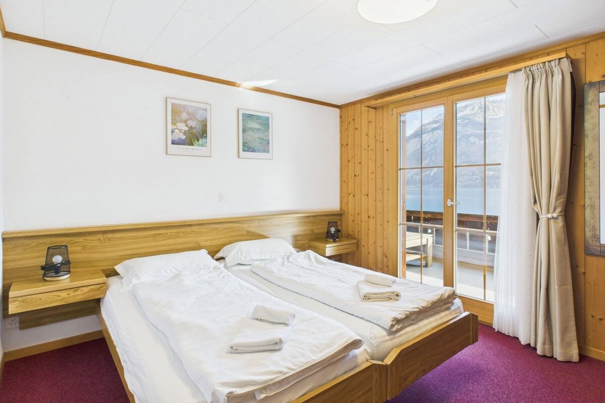 A hotel room with two beds, a wooden headboard, a window with curtains, and two framed pictures on the wall.