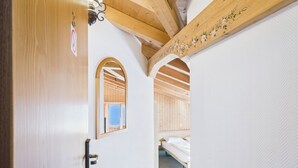 A hallway with a wooden door, a small arched window, and a bed in the background. - Hotel Wildbach Brienz (Brienz)
