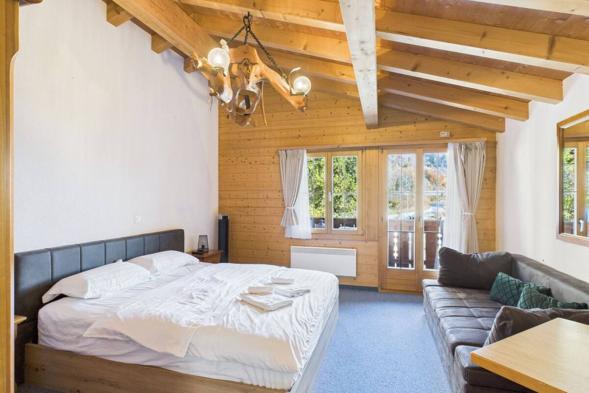 A bedroom with a bed, a wooden ceiling, a window with curtains, and a sofa.