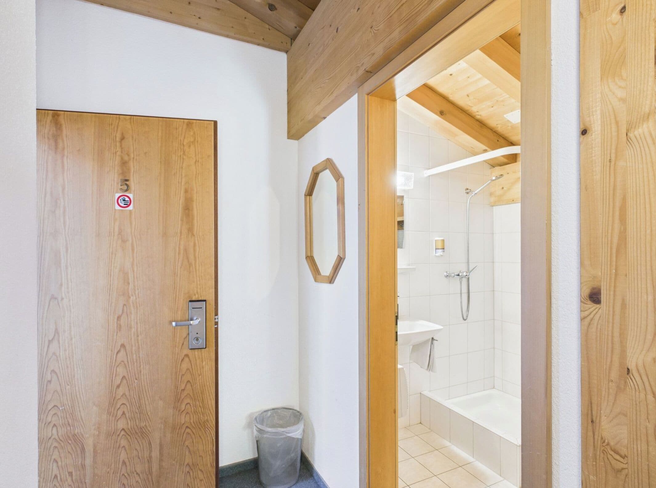 A wooden door with a number 5 sign, a trash bin, and a shower area with a bathtub.