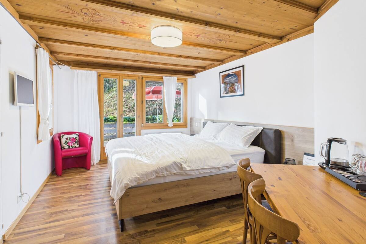 A bedroom with a wooden ceiling, a bed, a dining table, and a red chair.